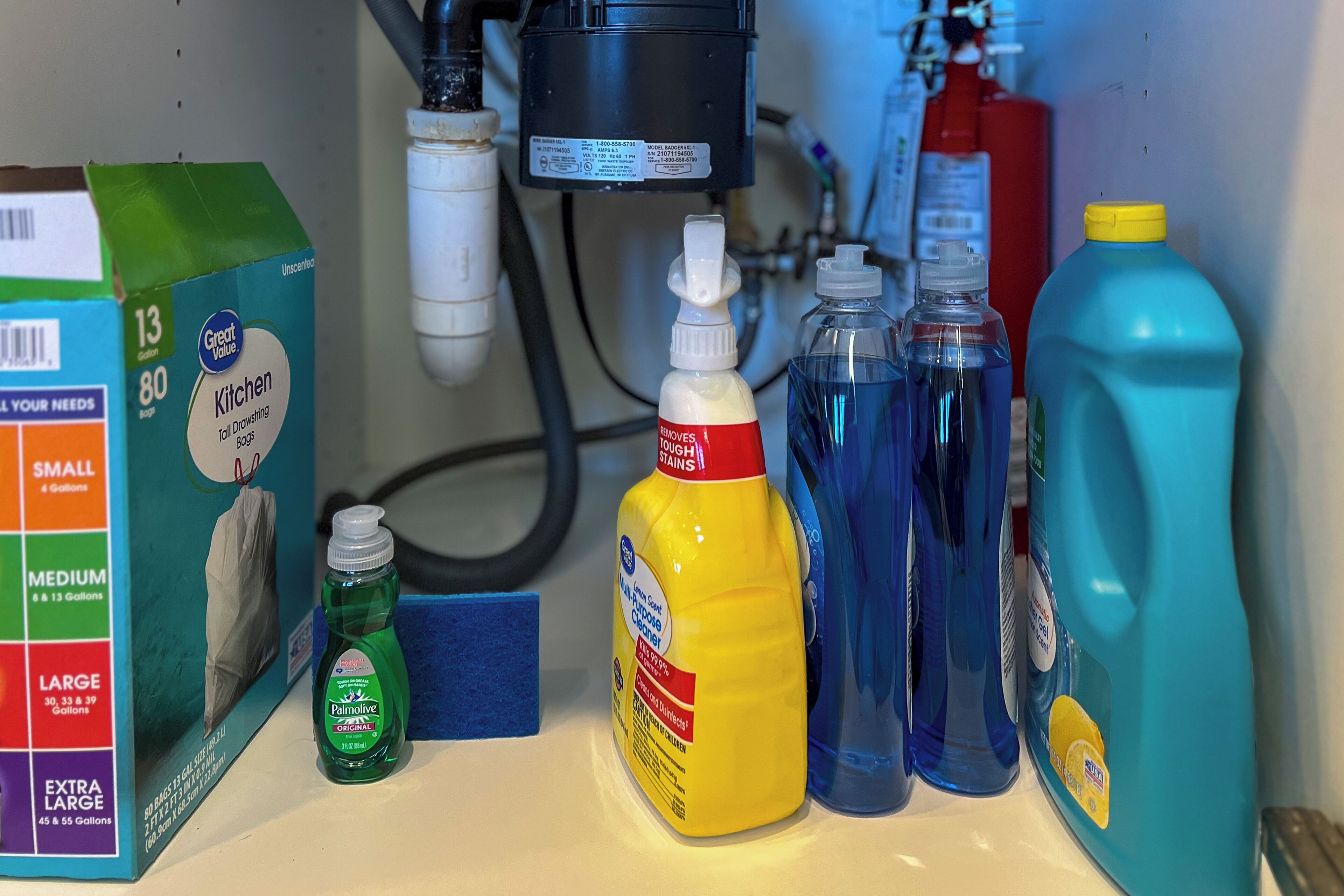 A kitchen sink area with cleaning supplies including a box of dish soap, a bottle of dishwashing liquid, and a blue detergent bottle.