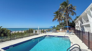 Een zwembad met helderblauw water, omringd door ligbedden en parasols, met uitzicht op de oceaan en palmbomen.
