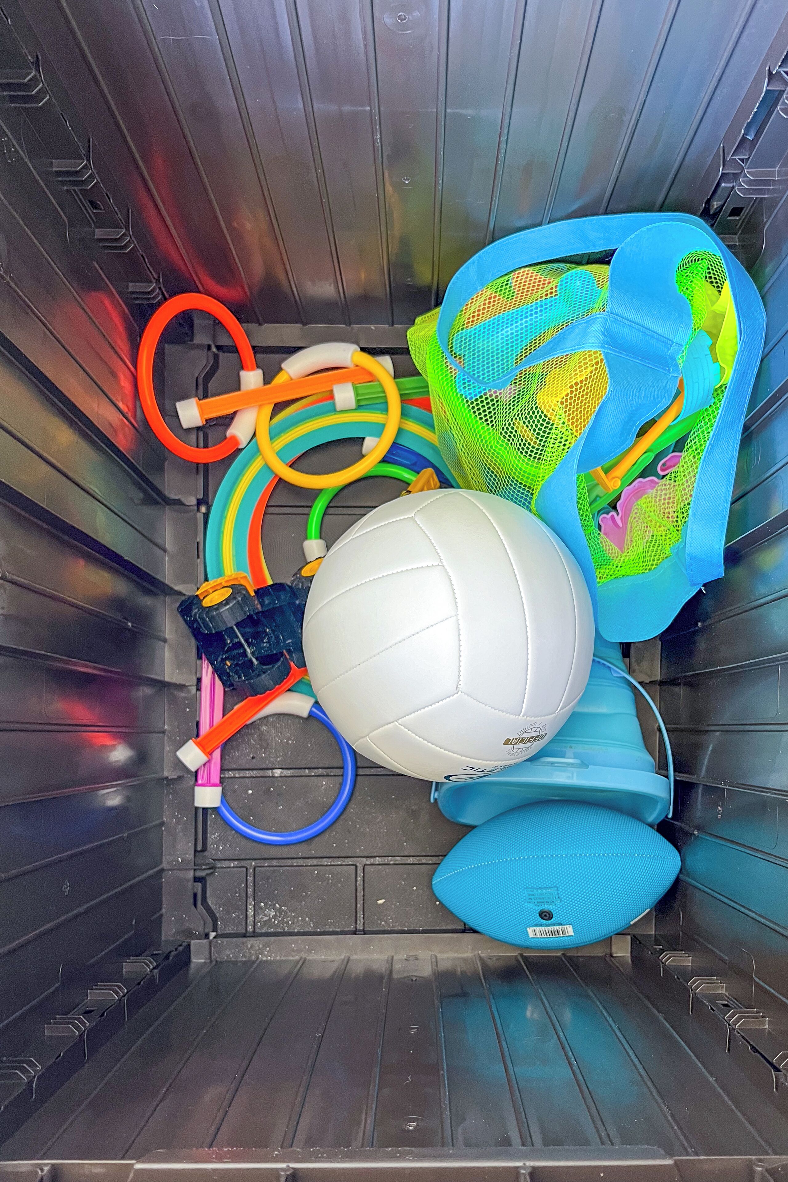Ein Lagerraum mit verschiedenen Gegenständen, darunter ein weißer Volleyball, eine blaue Netztasche und farbige Schläuche.