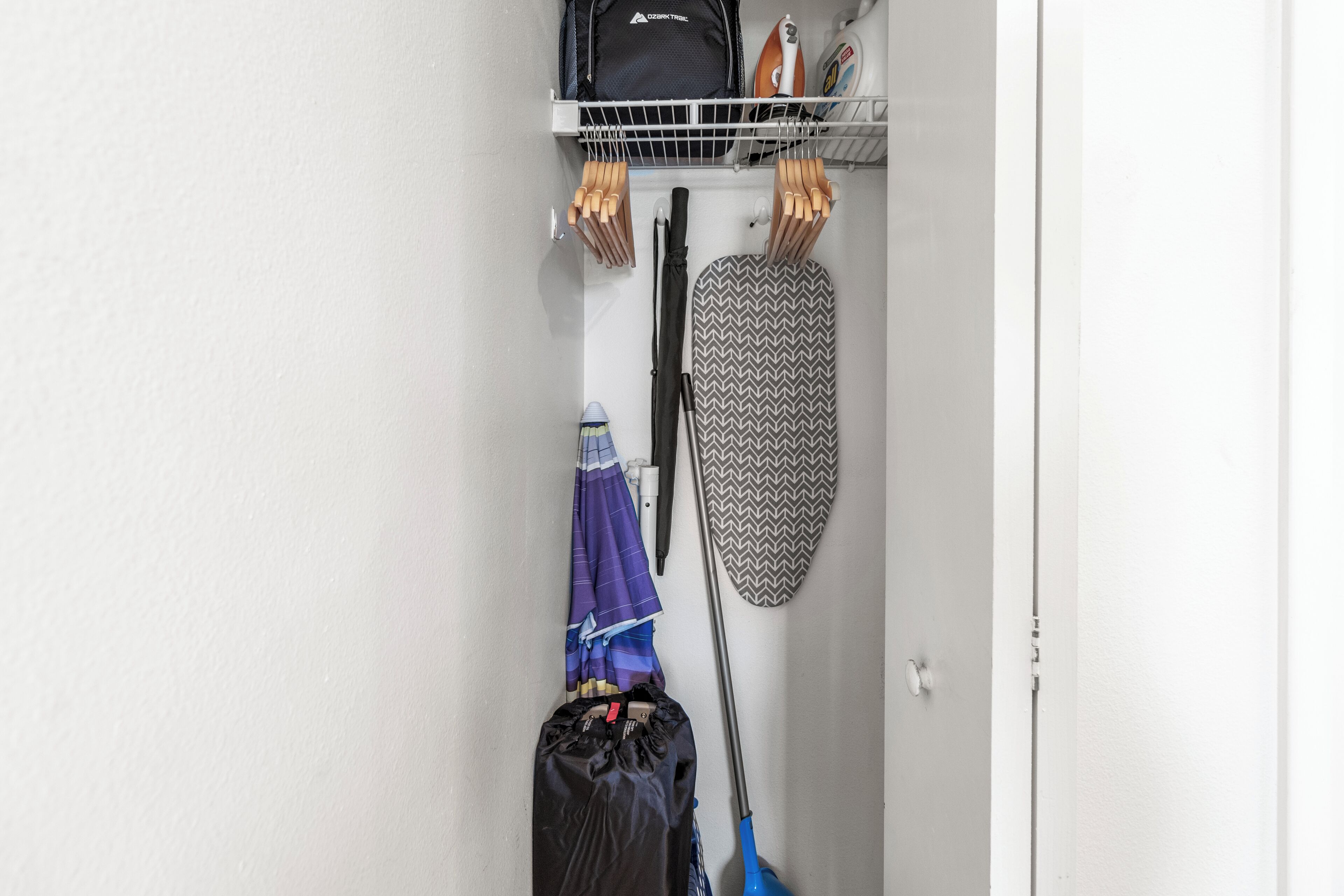 A storage area with a hanging iron, ironing board, and a mop.