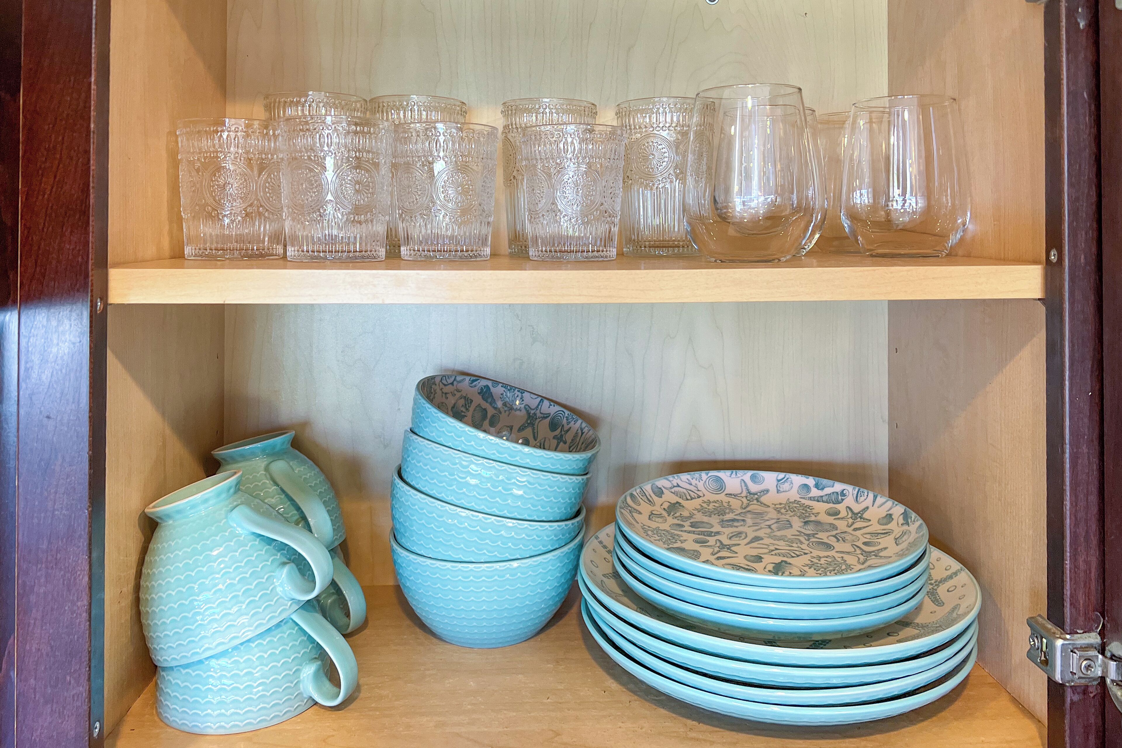 Un meuble de rangement avec des verres transparents et des assiettes en céramique bleue.