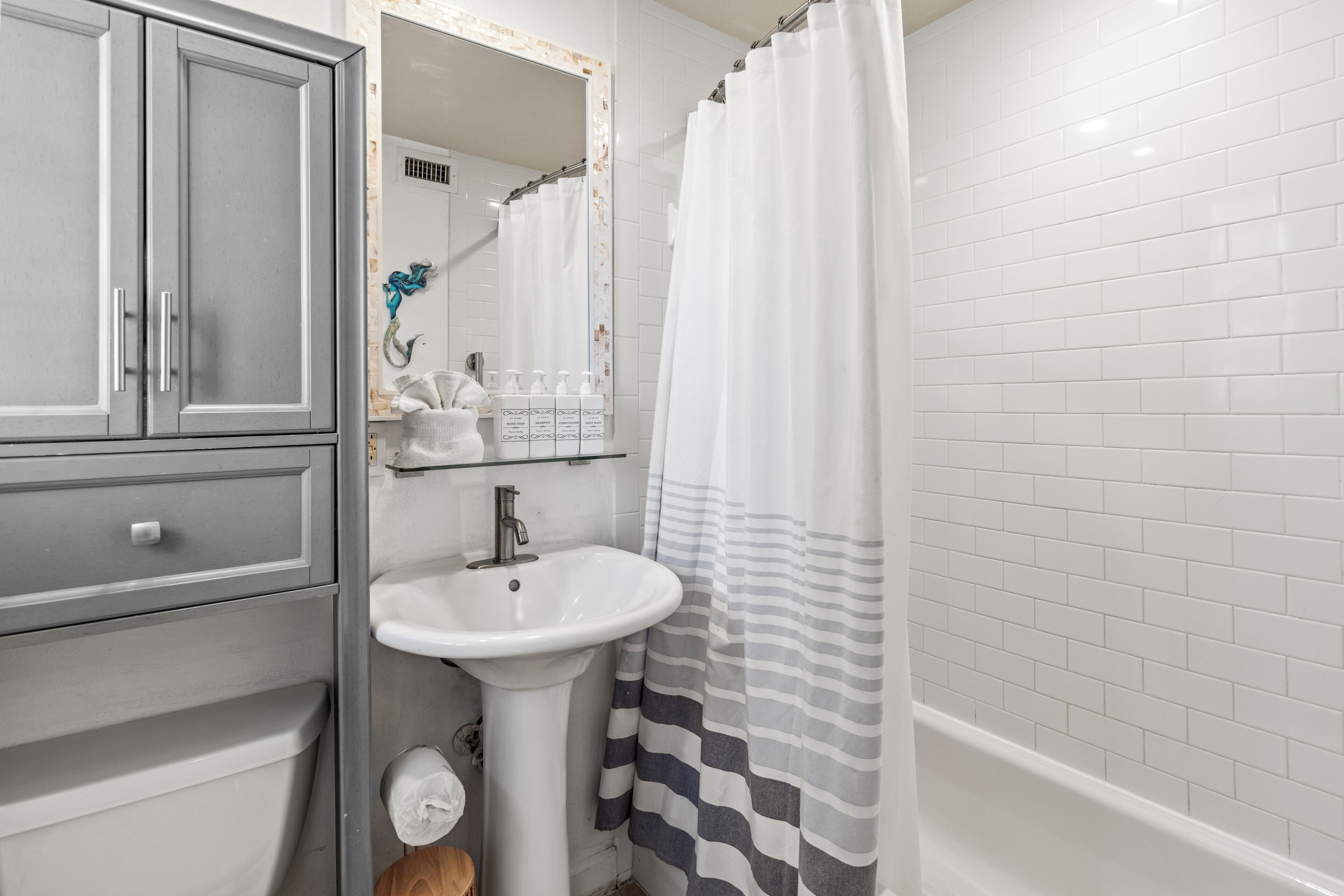 Une salle de bain avec un meuble gris, un lavabo blanc et un rideau de douche à rayures.