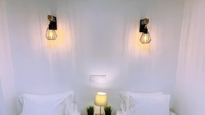 A hotel room with two single beds, a small bedside table with a lamp, and two wall-mounted light fixtures.
