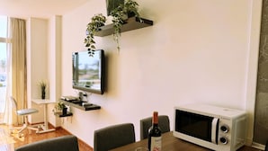 A modern dining area with a wooden table, chairs, a TV mounted on the wall, a microwave, and a wine bottle.