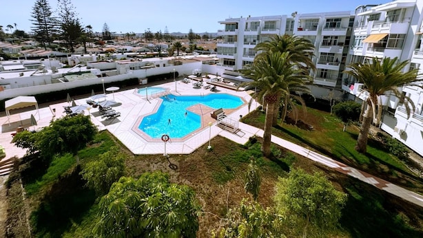 A modern hotel with a central swimming pool, surrounded by palm trees and a landscaped garden.