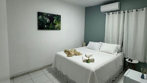 Une chambre d’hôtel bien rangée, avec un lit, une petite table de chevet, un climatiseur fixé au mur et une fenêtre avec des rideaux.