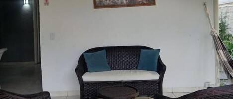 A covered outdoor seating area with wicker furniture and a painting on the wall.