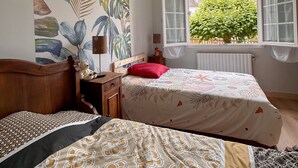 A bedroom with two beds, a large window with curtains, a radiator, and a wall with a tropical leaf pattern.