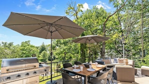 An outdoor patio with a grill, dining table, chairs, and umbrellas.
