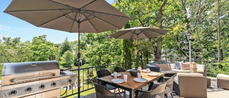 An outdoor patio with a grill, dining table, chairs, and umbrellas.