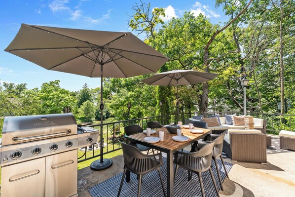 Un patio exterior con una parrilla, mesa de comedor, sillas y sombrillas.