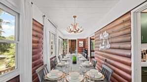 A dining area with a long table set for a meal, surrounded by wooden walls and large windows.