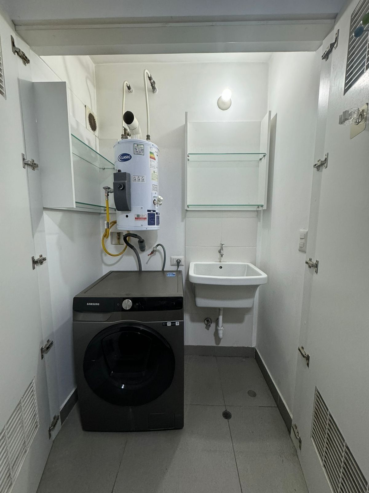 A compact bathroom with a washing machine, a built-in sink, and a glass shelf.