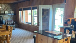 Ett kök med en köksö i trä, en vägg i sten och stora fönster.