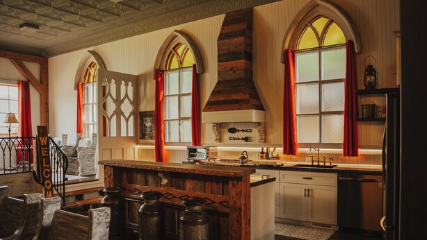 A kitchen with a wooden island, large windows with red curtains, and a stone fireplace. - Island View Cottage: Waterfront-BBQ-Sauna-AC-Wifi, Island View Cottage (Flatlands)