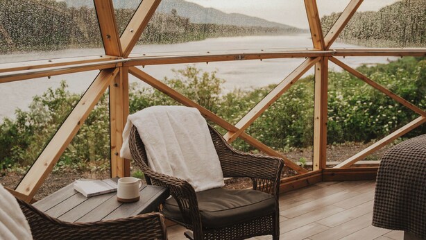 Una terraza de madera con mobiliario de mimbre y vistas a un lago y montañas.