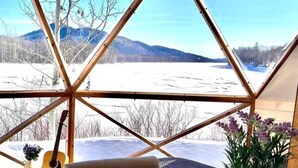 Un comedor con una mesa dispuesta para el desayuno, una guitarra y vistas a un paisaje nevado a través de una estructura de ventana geométrica.