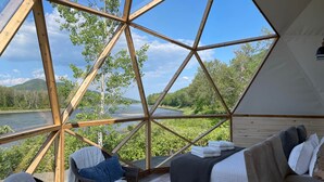 Una habitación en forma de cúpula geométrica con vistas a un río y un bosque.