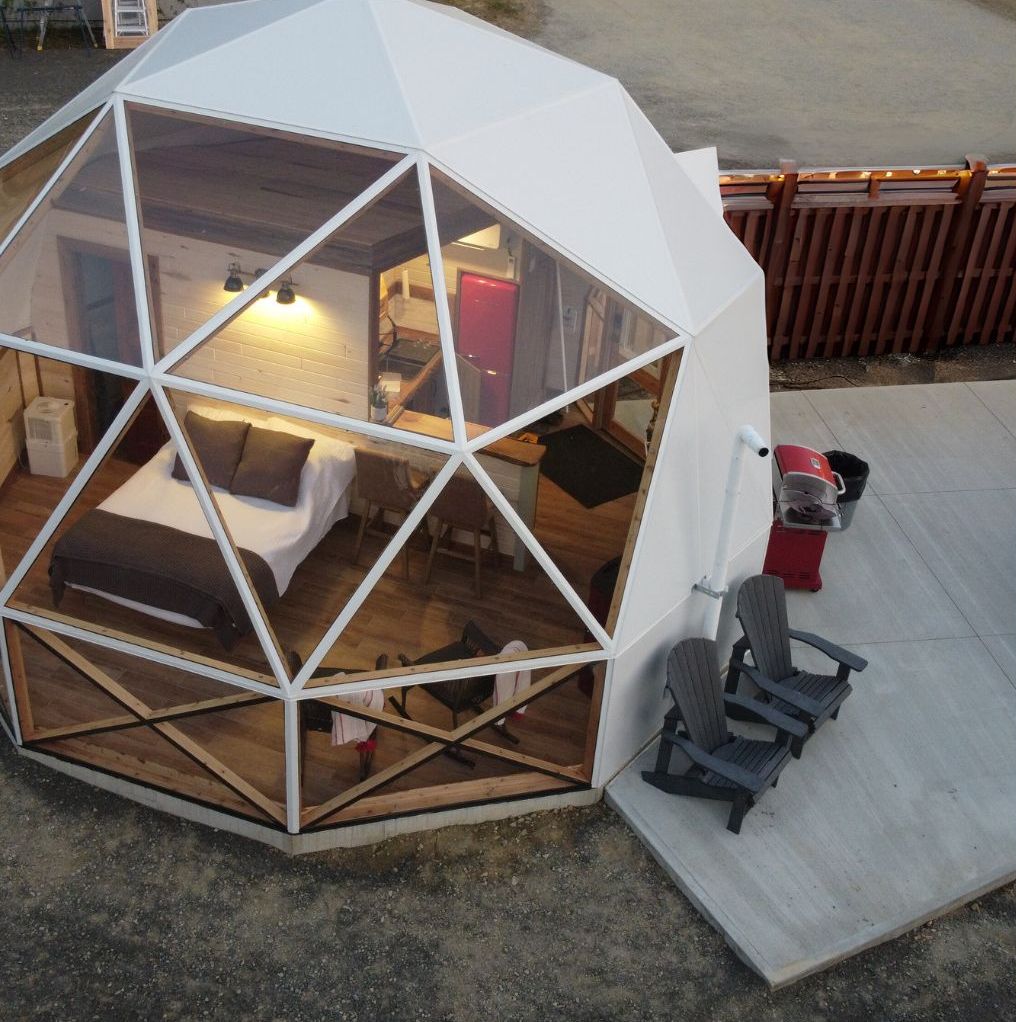 A geodesic dome structure with a bed, seating area, and a small kitchen.