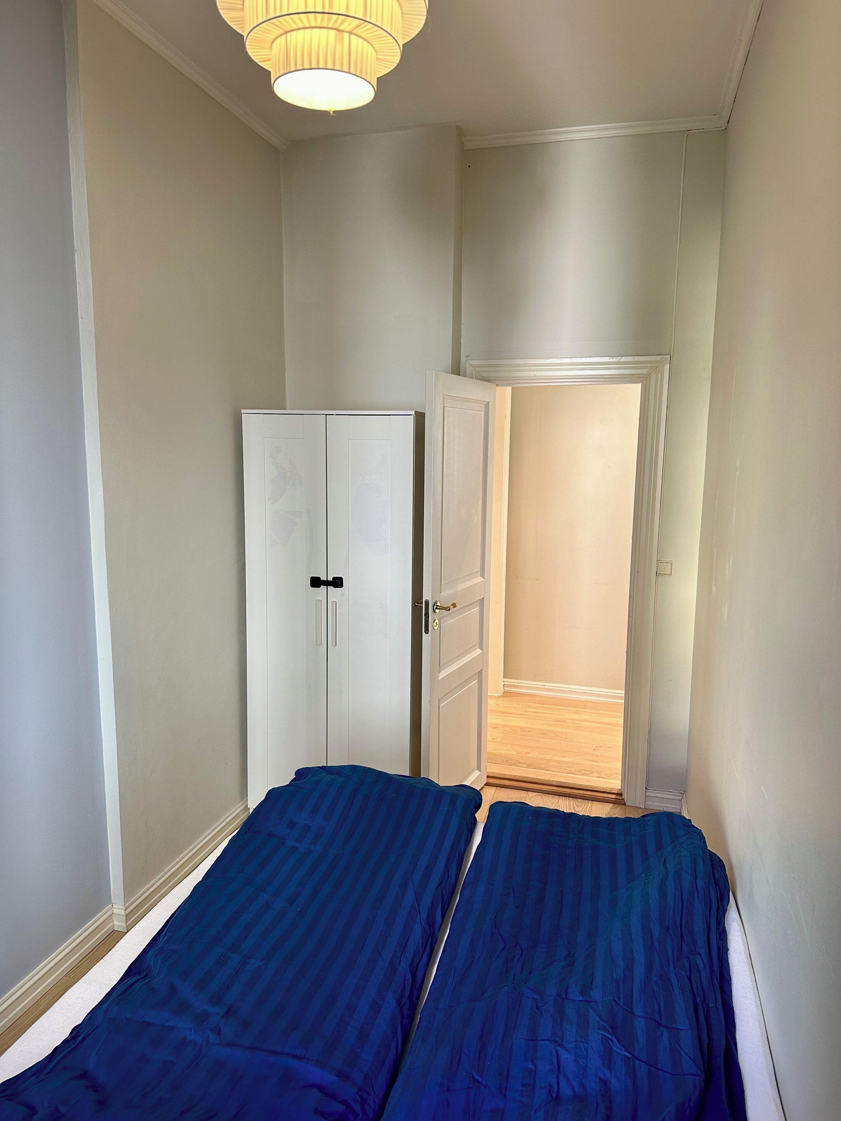 A narrow room with two beds, a wardrobe, and a door leading to another room.