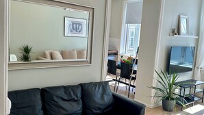 A modern living room with a black leather sofa, a large mirror, and a television on a wooden floor. - Classical 3 bedroom, 2 bath, minutes walk from Royal Palace, Shopping & Downtown (Oslo)