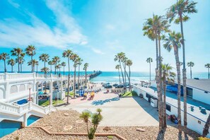A beachfront hotel with a pool, palm trees, and a pier extending into the ocean. - Epic Family Retreat, Hot Tub, Fire Pit, Near Legoland (Vista)