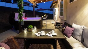 Un patio al aire libre con una mesa de madera preparada para dos, un jacuzzi y una zona de estar con cojines.