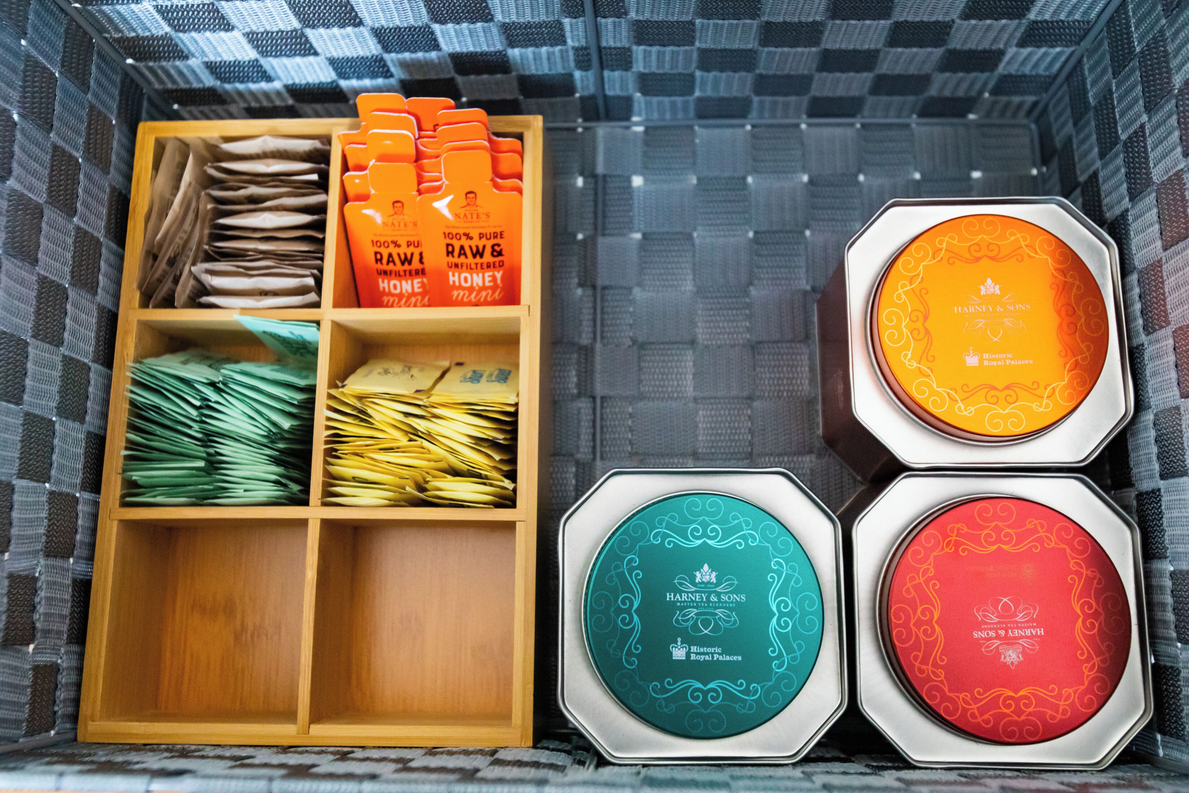 Ett förvaringsutrymme med hyllor av trä, där olika föremål förvaras, bland annat hopvikta papper och orangefärgade lådor märkta med texten "RAW & HONEY".