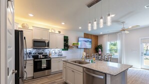 Une cuisine moderne dotée d’appareils électroménagers en acier inoxydable, d’un grand îlot central et de luminaires suspendus.