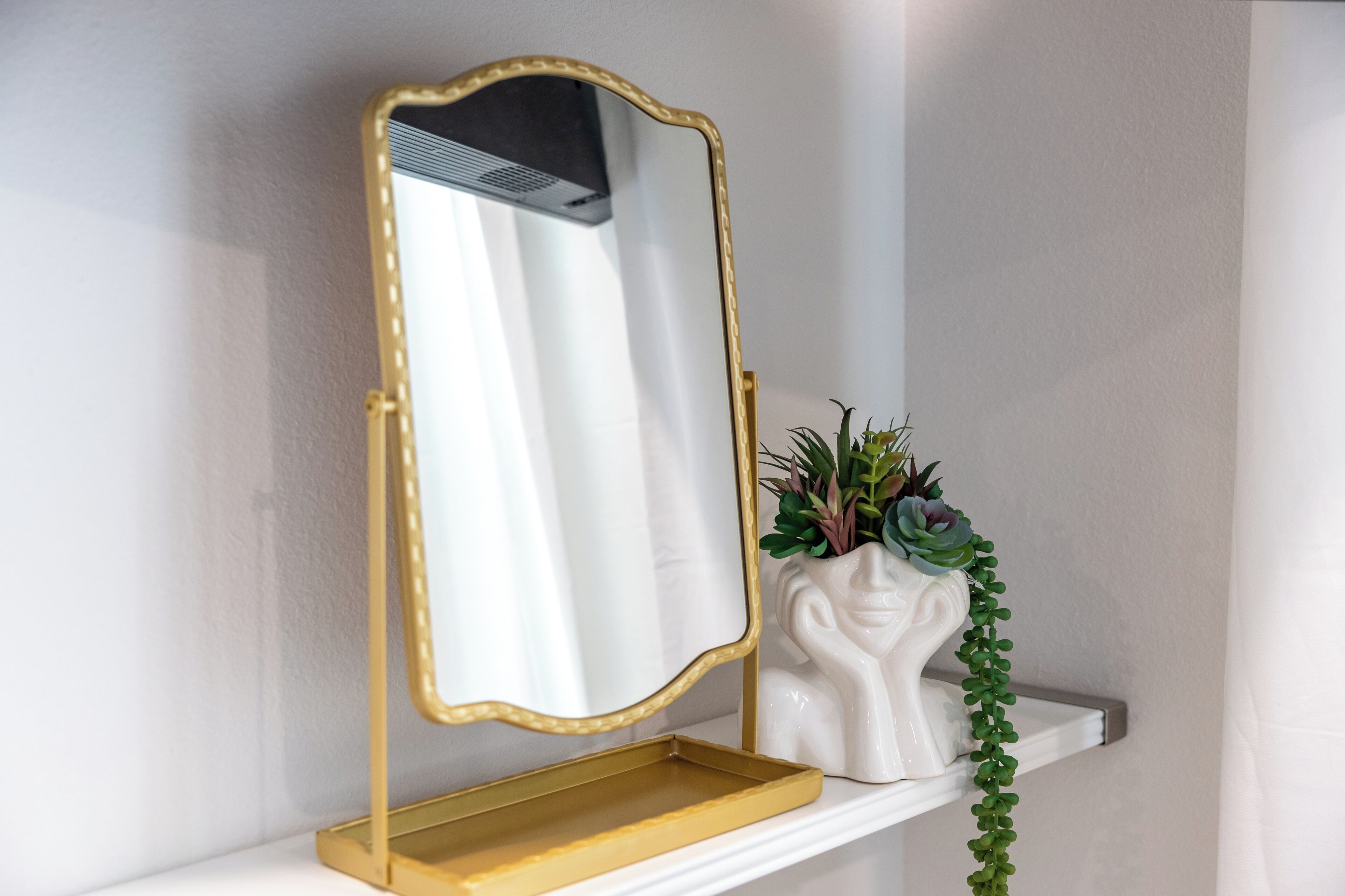 A mirror with a gold frame on a white shelf.
