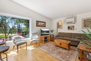 Ett modernt vardagsrum med ett stort fönster, en tv, en soffa, ett soffbord och en växt.