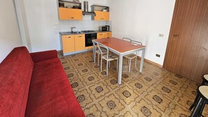 A compact kitchen with a dining area, a red sofa, and patterned floor tiles. - Guests' Nest (Castellammare del Golfo)