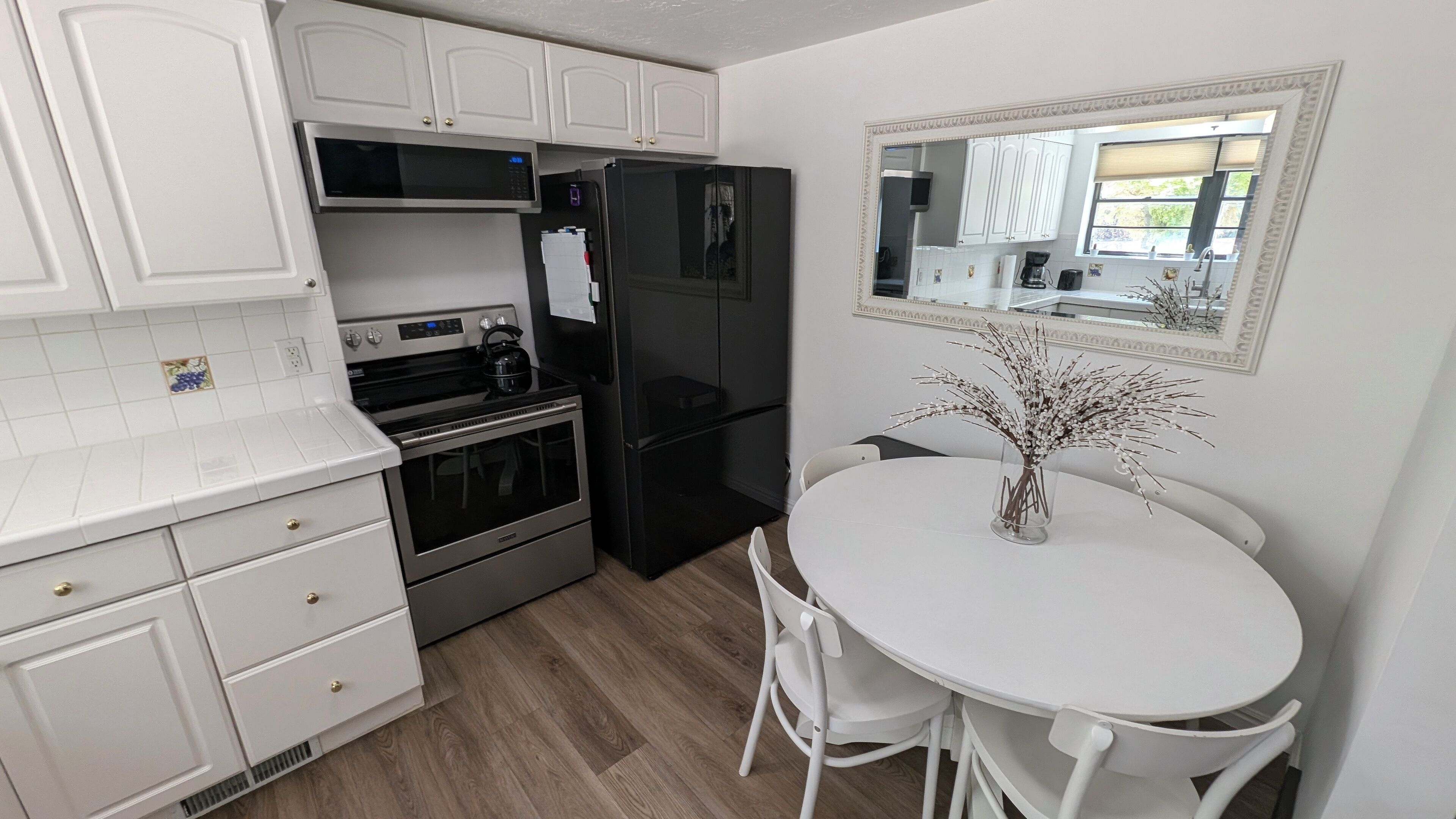 A kitchen with white cabinets, a black refrigerator, a stove, and a dining table with chairs.