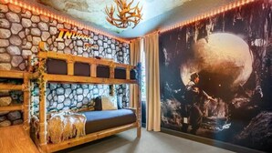 Un lit superposé avec un mur en pierre en arrière-plan, un lustre et une fresque représentant une scène de grotte.