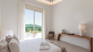 A hotel room with a large bed, a wooden bench, a chair, and a view of the countryside. - Villa Selena Antequera by Ruralidays (Málaga)