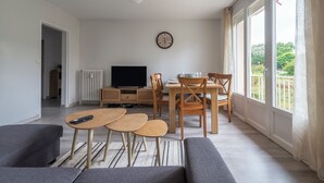 Ett modernt vardagsrum med en tv, trämöbler och en balkong med gardiner.