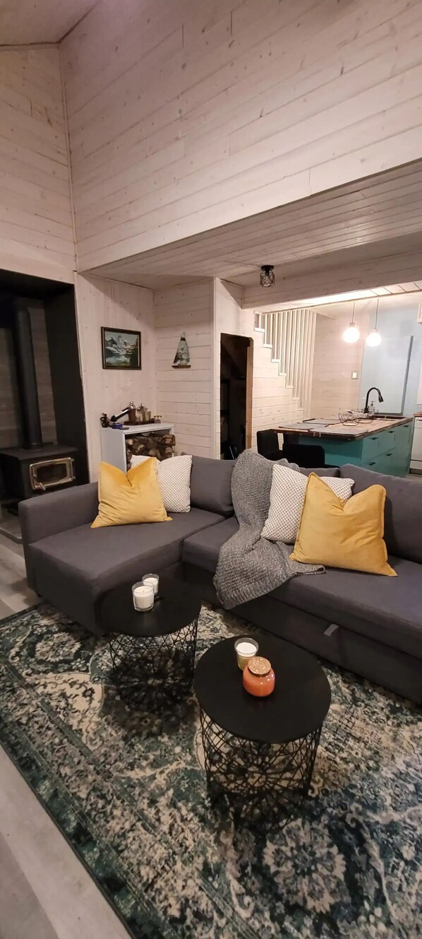 A modern living room with a grey sofa, yellow cushions, a patterned rug, and a small round table with candles. - 4 Season Lakefront Cottage with Hot Tub (Little Deer Lake)