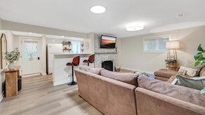 A modern living room with a sofa, a fireplace, and a TV mounted above it. - Your Peaceful Minnetonka Home Base • Comfortable, Cozy & Conveniently Located (Minnetonka)