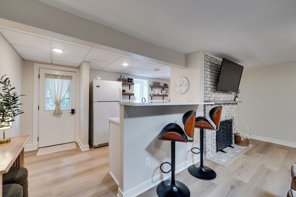 A modern kitchen with a white island, bar stools, a built-in TV, and a fireplace.