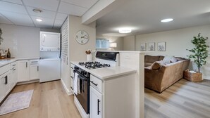 Une cuisine moderne avec des meubles blancs, une cuisinière et un réfrigérateur. On y trouve également un coin repas avec un canapé marron et une plante.
