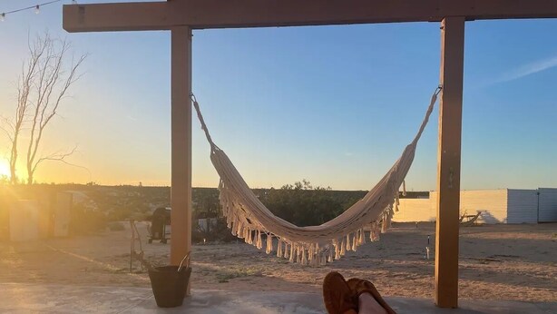 A hammock under a pergola with a view of the sunset and distant buildings.