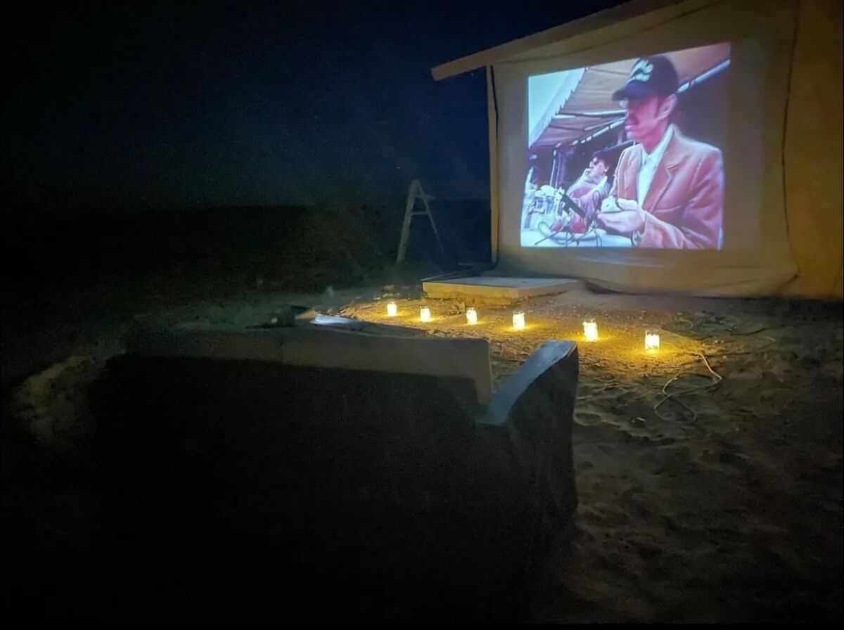 A projection screen displaying a movie scene on a sandy surface with candles arranged in front.
