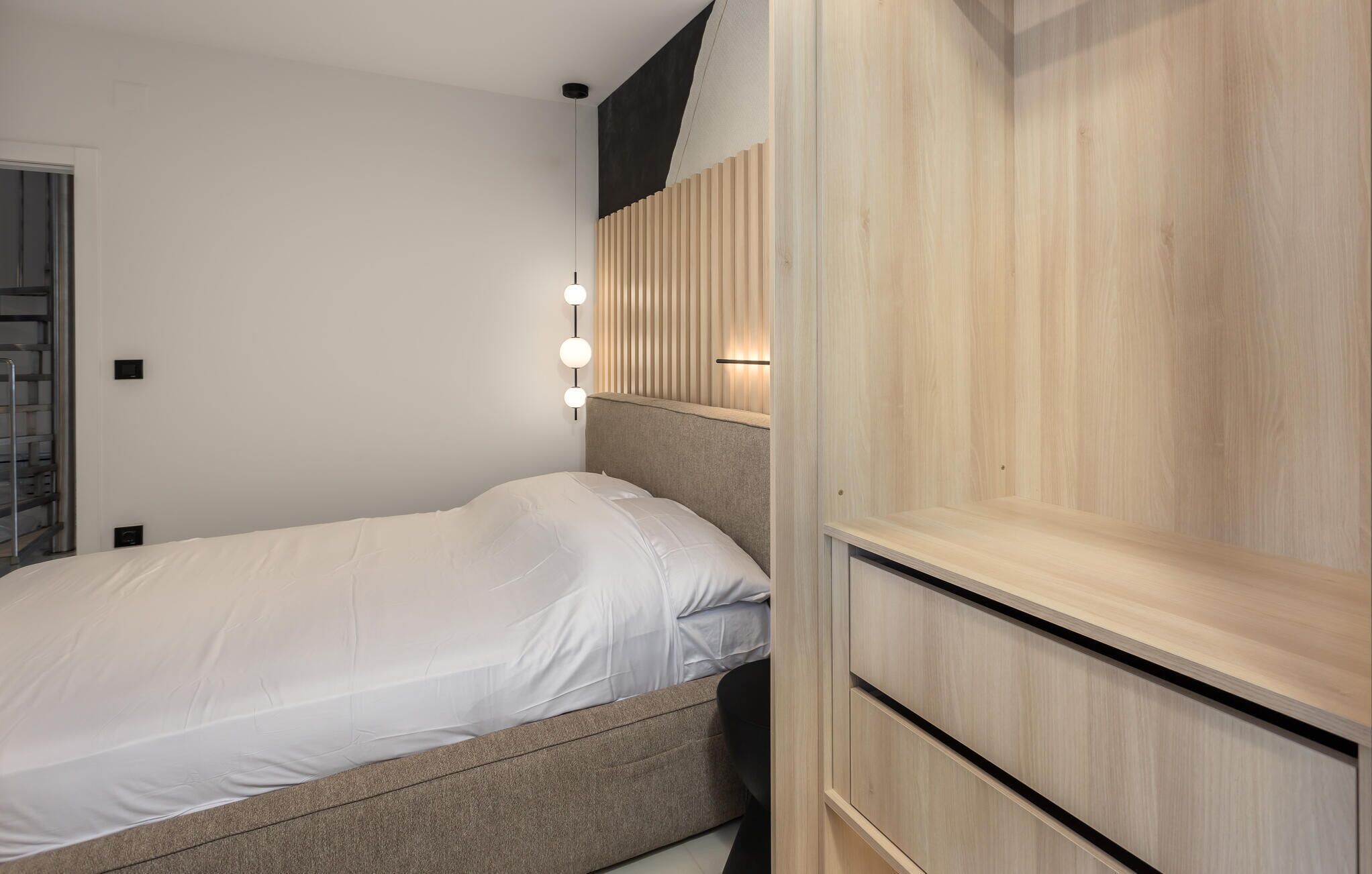 A bedroom with a bed, a wooden wardrobe, and a wall-mounted light fixture.