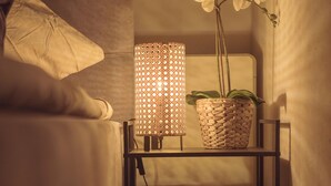 Un dormitorio con una cama, una lámpara de noche, una orquídea en maceta y un par de zapatillas deportivas en un estante.