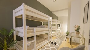 Habitación con literas, una pequeña mesa y silla, una planta en maceta y una alfombra estampada.