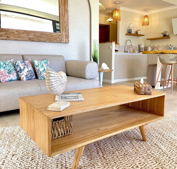 Een moderne zithoek met een houten salontafel, een grijze bank met gekleurde kussens, een gevlochten mand en een tijdschrift.