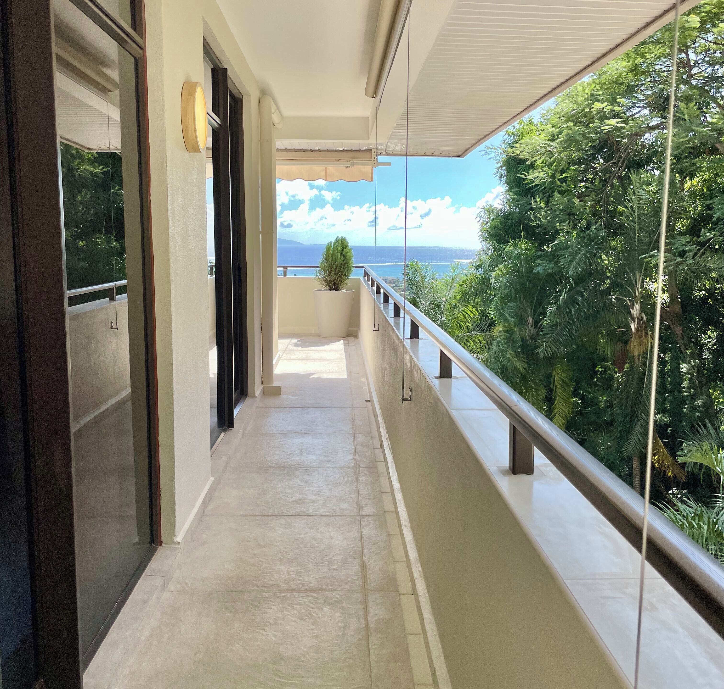 Un couloir donnant sur un balcon, avec une plante en pot et une vue partielle sur la mer.
