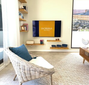 A modern living room with a wicker chair, a flat-screen TV, and a patterned rug.