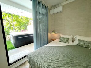 A bedroom with a bed, a nightstand, a window with curtains, and an air conditioning unit.