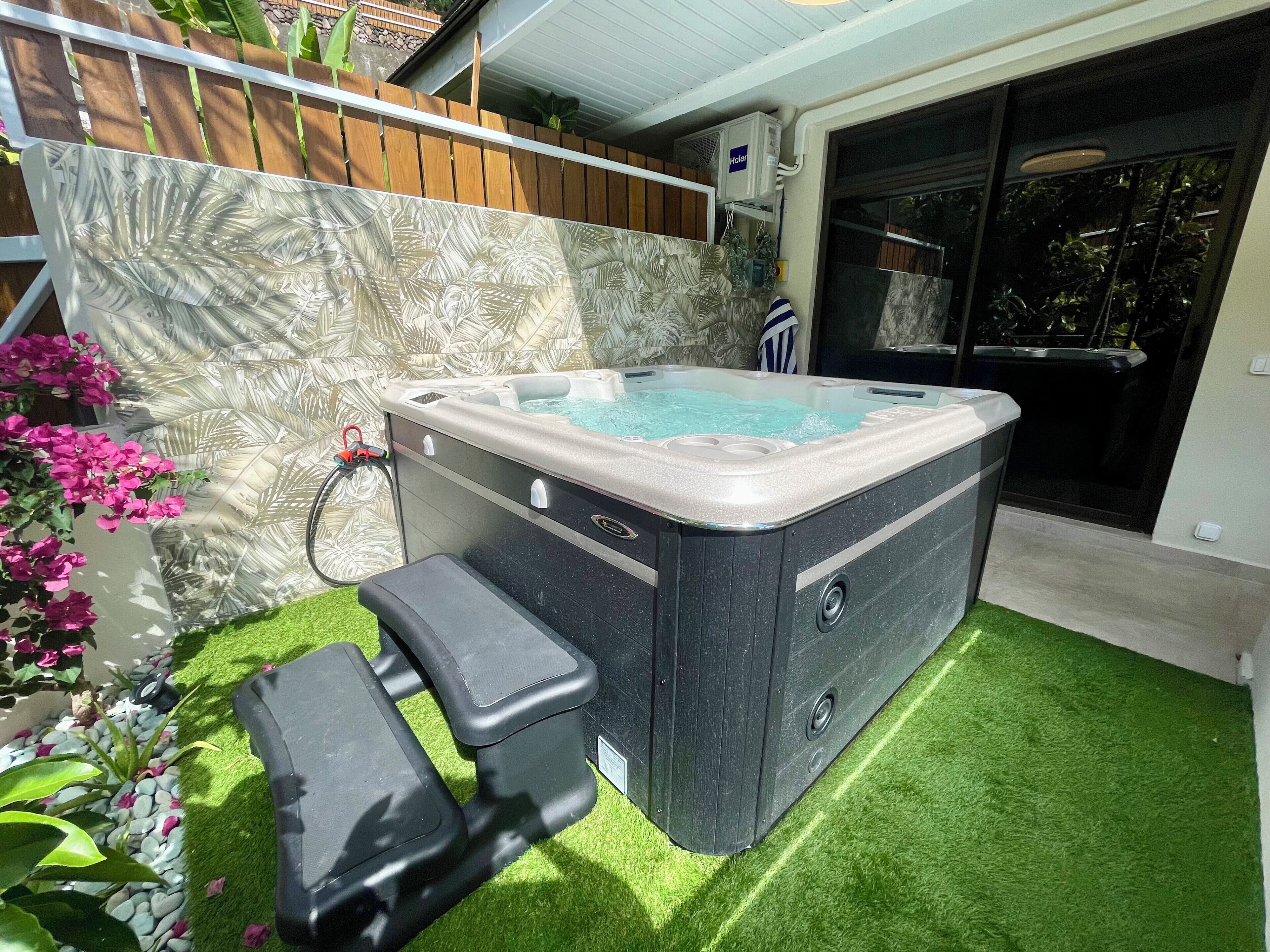 A hot tub with a built-in seat, surrounded by artificial grass and a decorative wall.